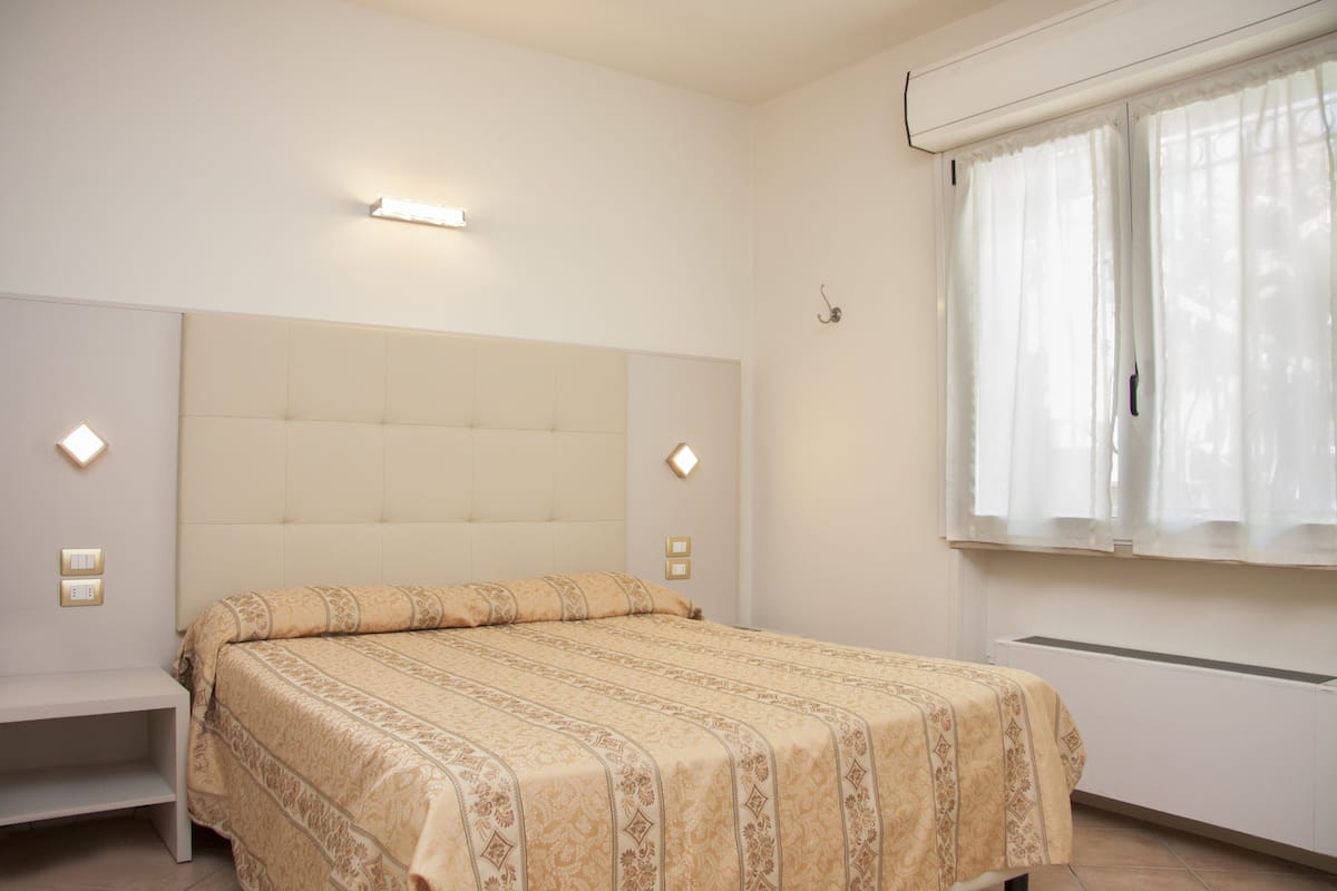 A bedroom with a bed, bedside tables, a window with curtains, and wall-mounted lights.