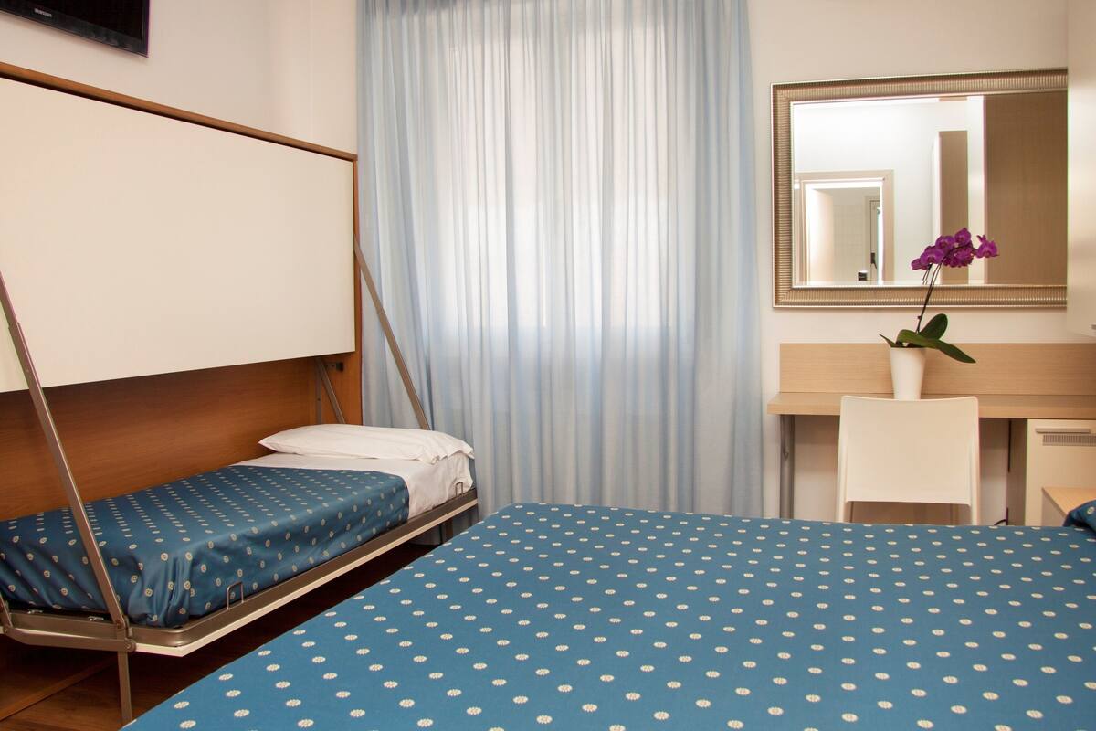 A bedroom with a bed, a desk, a chair, a hanging chair, and a mirror.