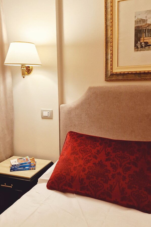 A hotel room with a bed, a nightstand with a lamp, a framed picture on the wall, and a red patterned pillow. - Boncompagni Suite (Rome)