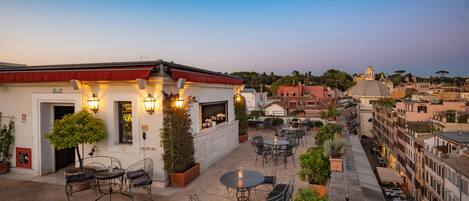 A rooftop patio with outdoor seating, a bar, and a view of the cityscape.