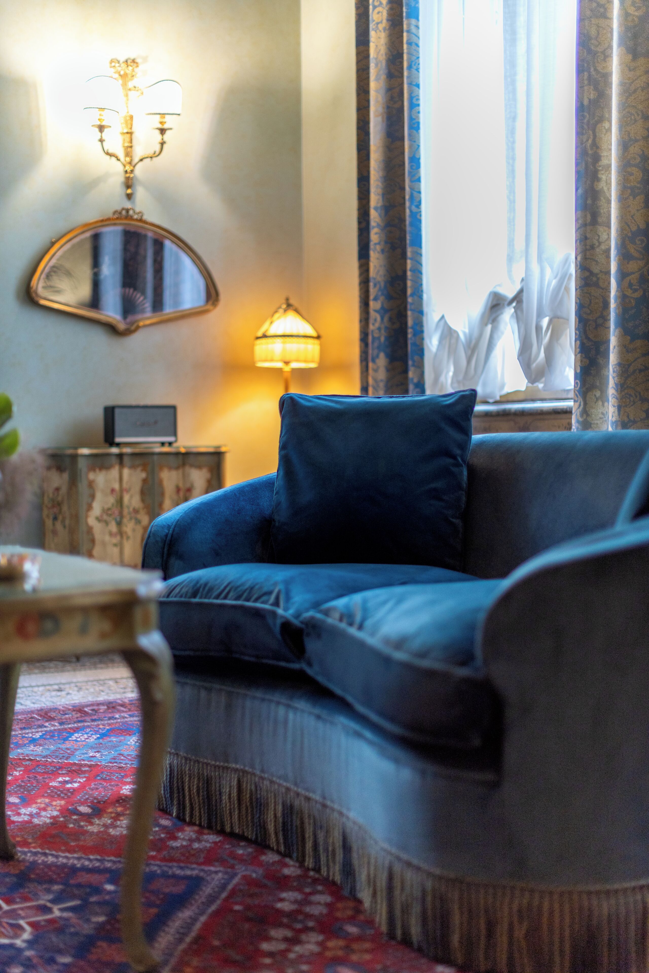 En hyggelig stue med en blå sofa, et lille bord med en lampe og et spejl på væggen.