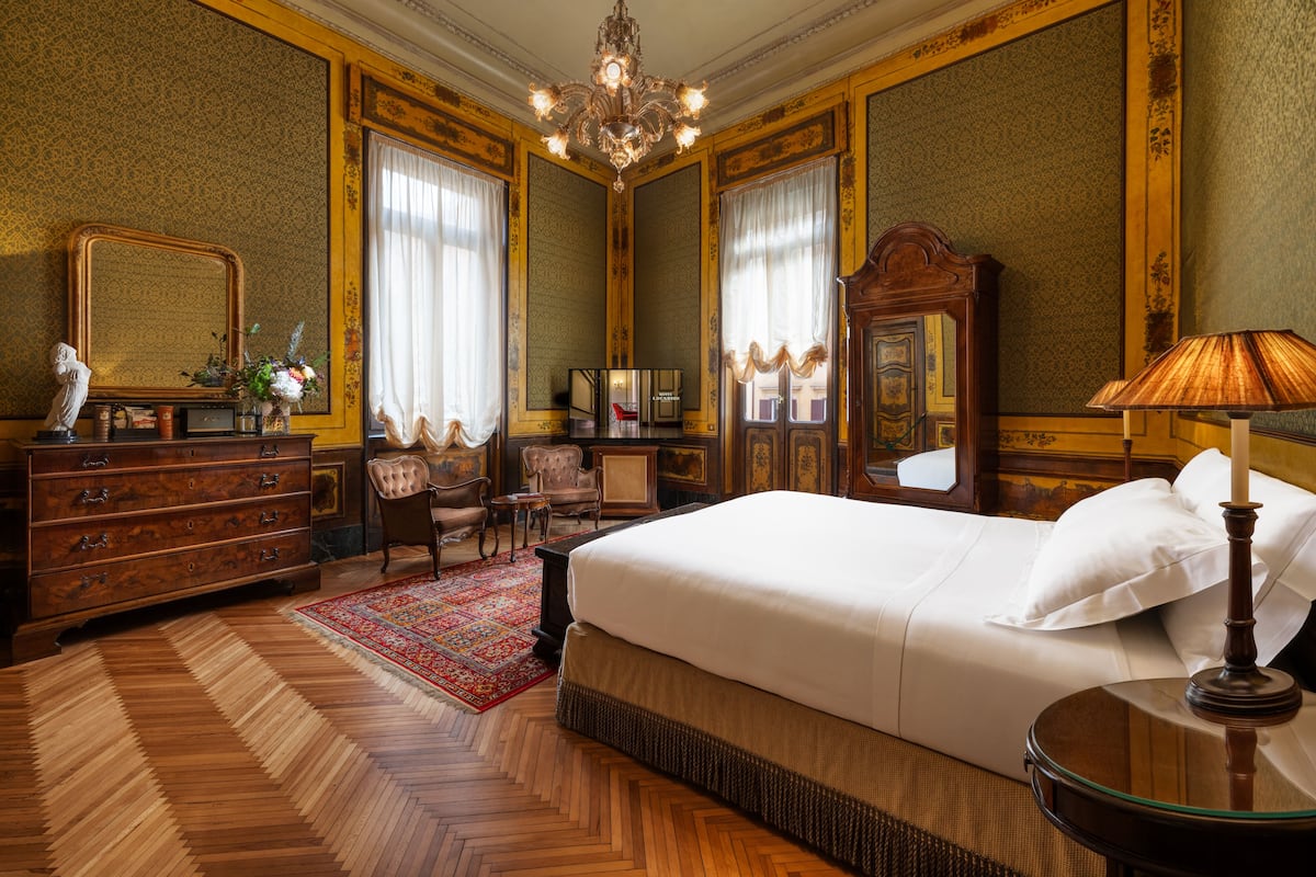 A luxurious bedroom with a large bed, a dresser, a mirror, and a chandelier.