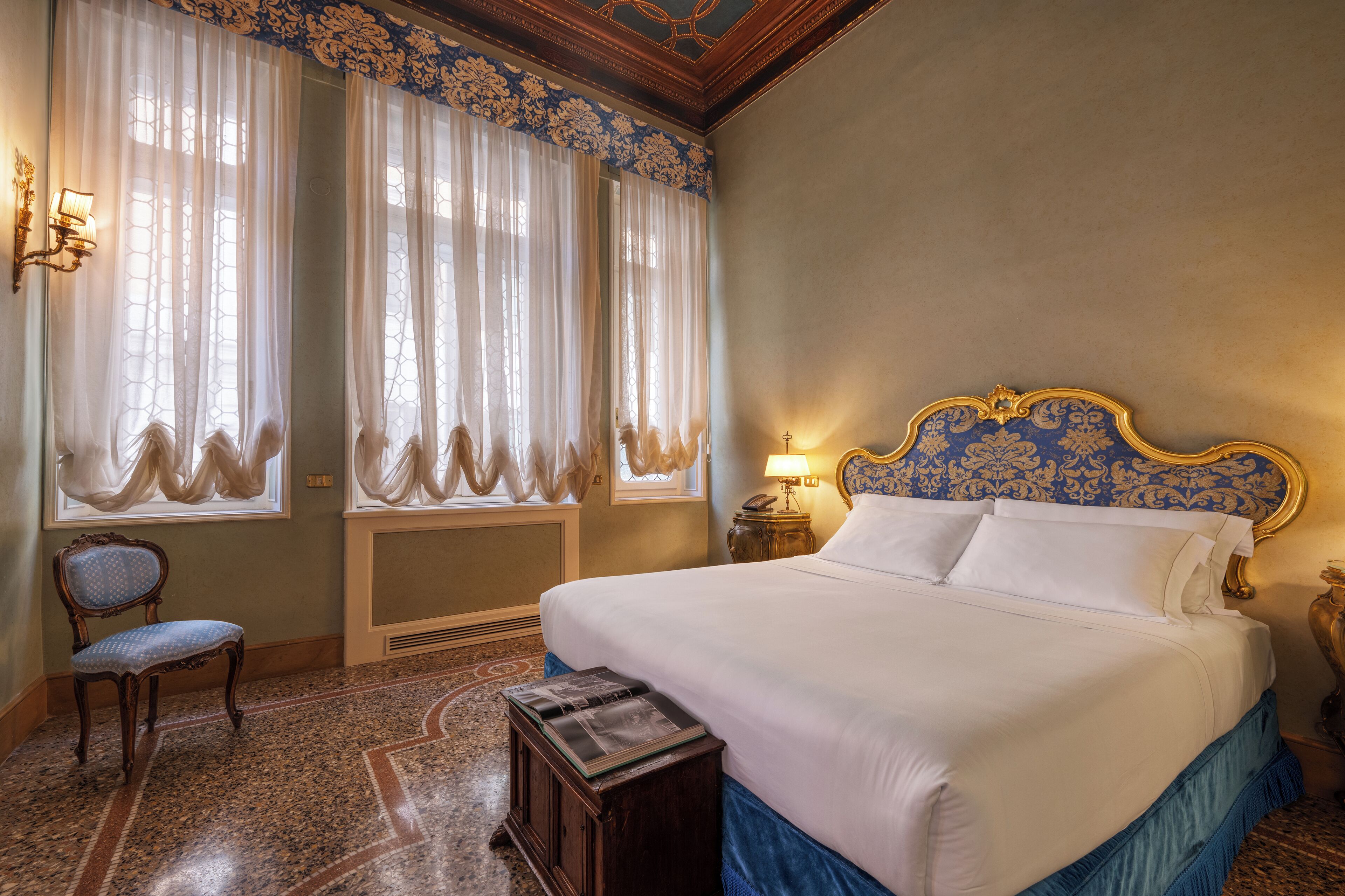 Une chambre à coucher avec un grand lit, une chaise, une table de chevet avec une lampe et une fenêtre avec des rideaux.