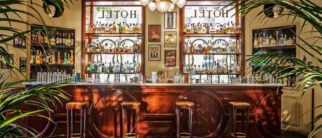 Zona de bar con mostrador de madera, varios taburetes y estantes llenos de botellas.