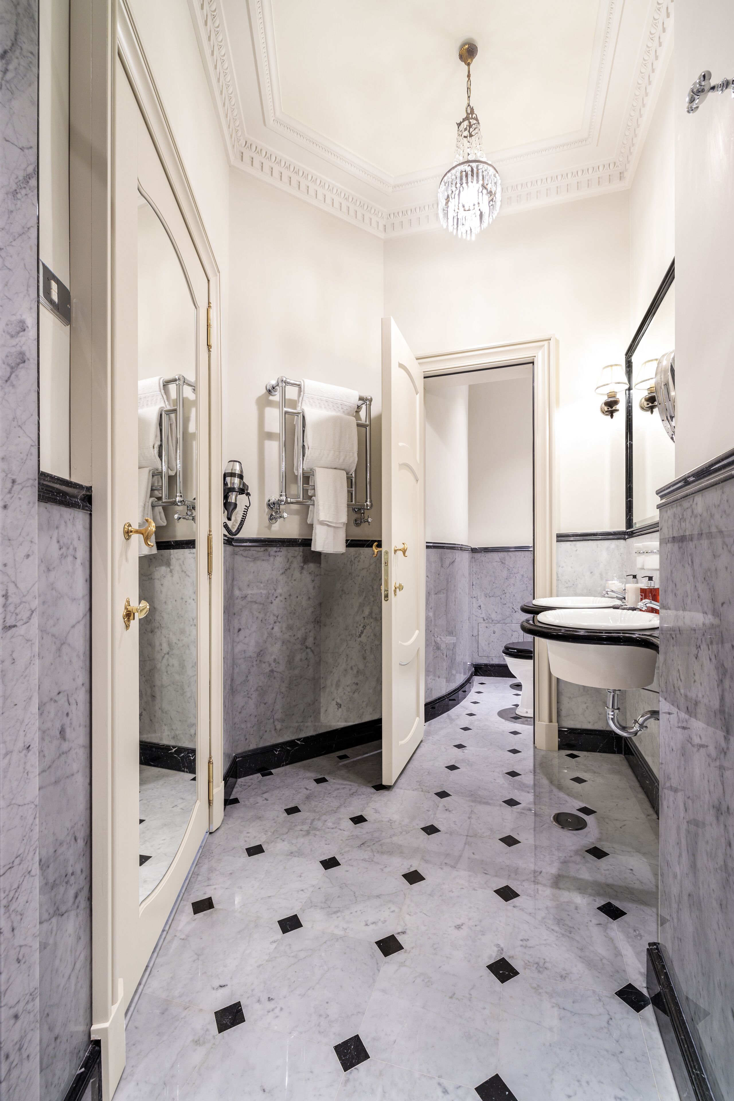 Une salle de bain avec un sol en marbre, un lustre et un double vasque.