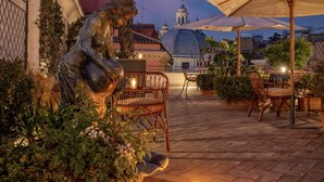 Patio esterno con una statua, piante in vaso e un tavolo con sedie.