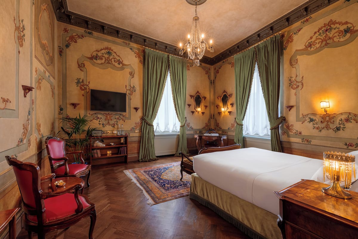 A classic hotel room with a large bed, a television, a desk, and a chandelier.
