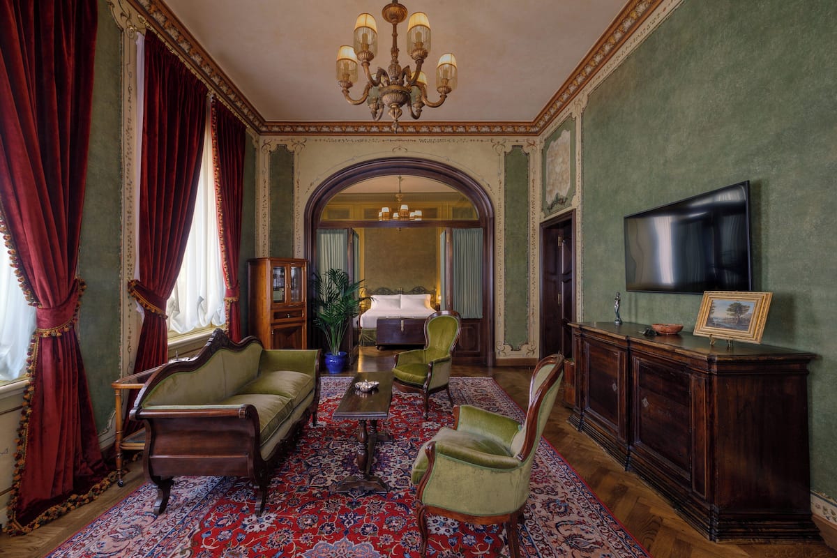 A room with a classic design, featuring a sofa, armchairs, a wooden cabinet, and a television.