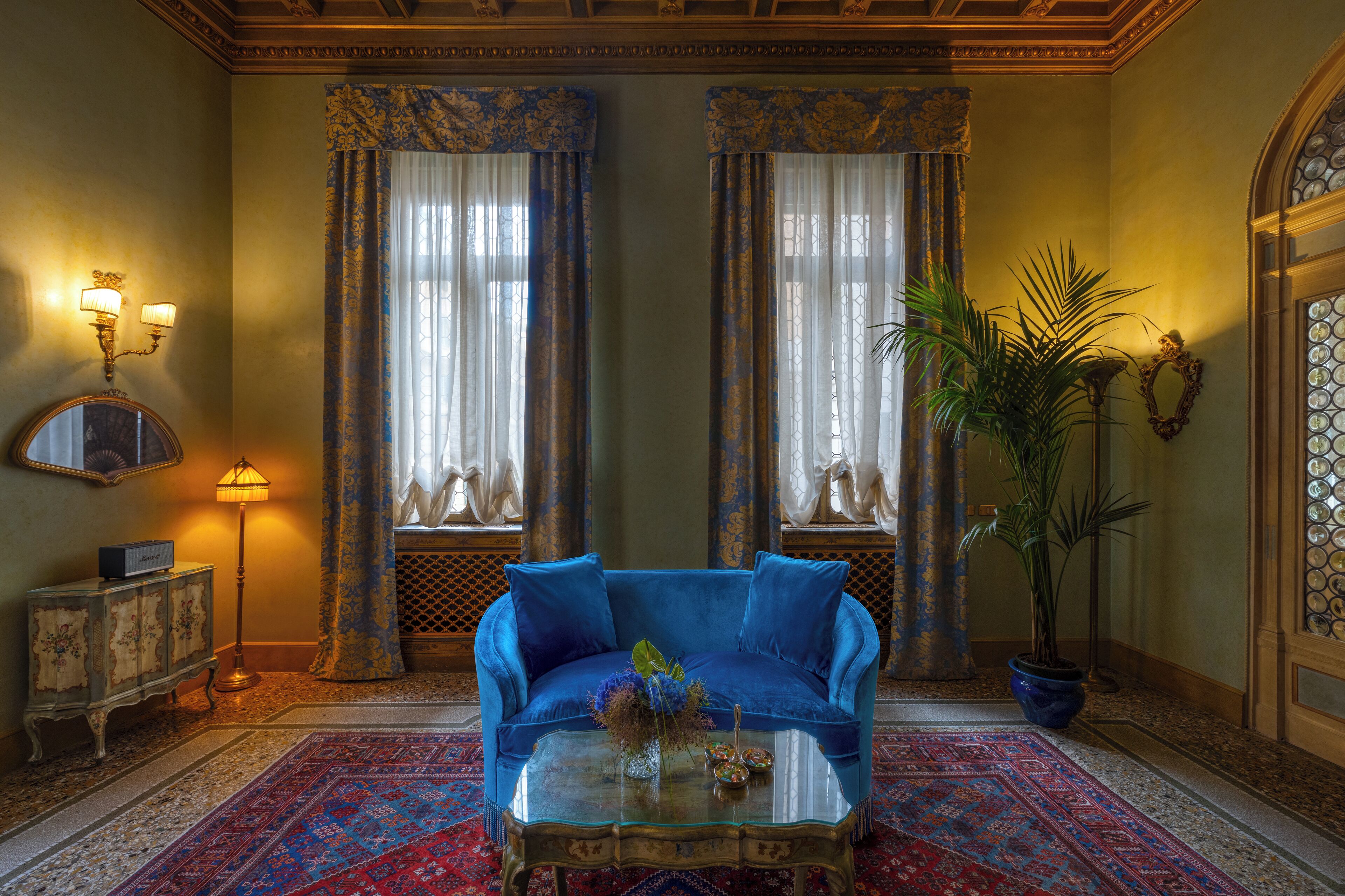A room with a blue sofa, a glass coffee table, a potted plant, and a decorative mirror.