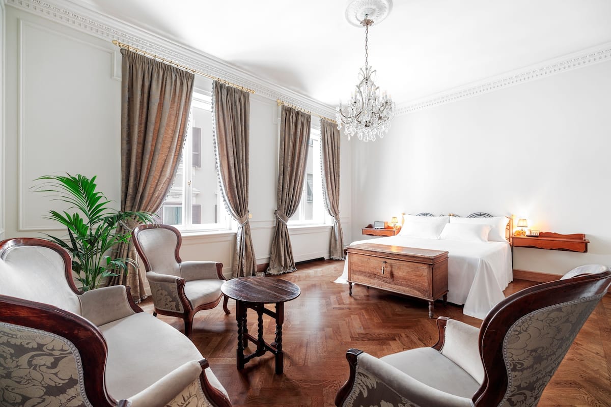 A hotel room with a bed, a wooden dresser, a round table, and two armchairs.