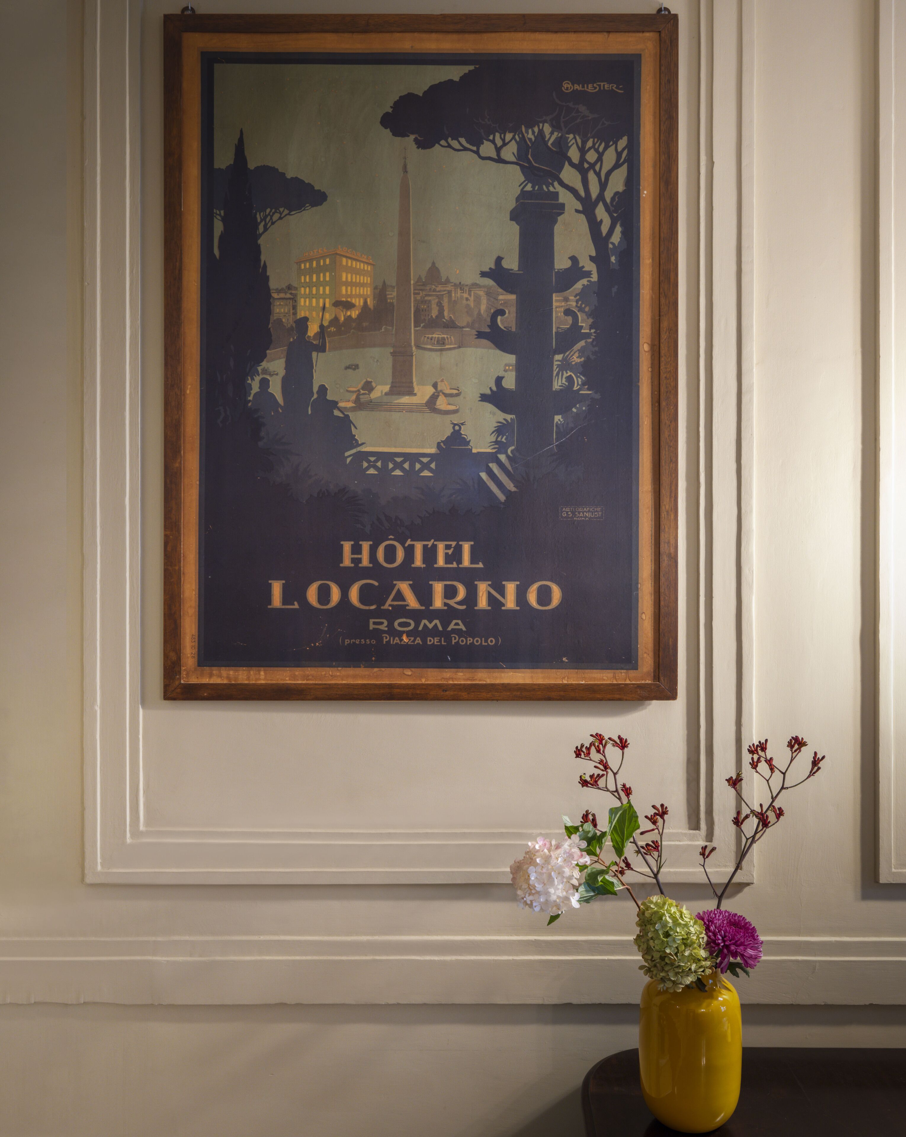 Póster enmarco del Hotel Locarno en Roma, con un florero sobre una mesa.