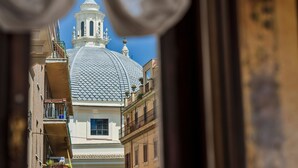 Vista attraverso una finestra su un edificio con cupola bianca e campanile, strada stretta e balconi.