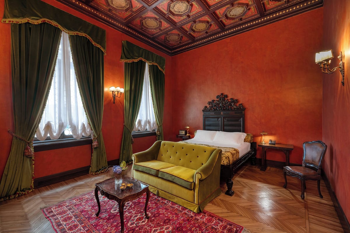 A room with a bed, a green sofa, a wooden table, and a red rug.