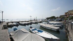 A marina with several boats docked, a paved walkway, and a building in the background. - Hotel Villa Rosa (Sirmione)