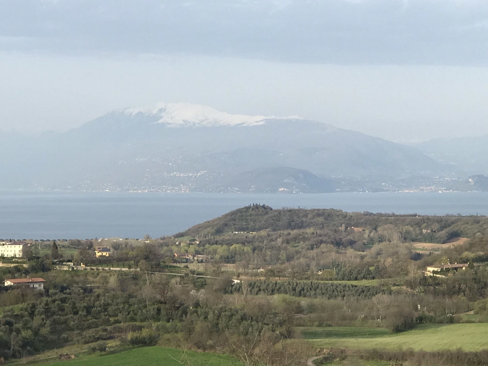 Een panoramisch uitzicht op een kustlandschap met een berg op de achtergrond, een waterlichaam en verspreide gebouwen.