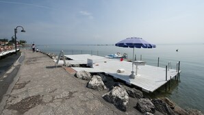 A pier with a metal roof, a blue umbrella, and a boat. - Hotel Villa Rosa (Sirmione)