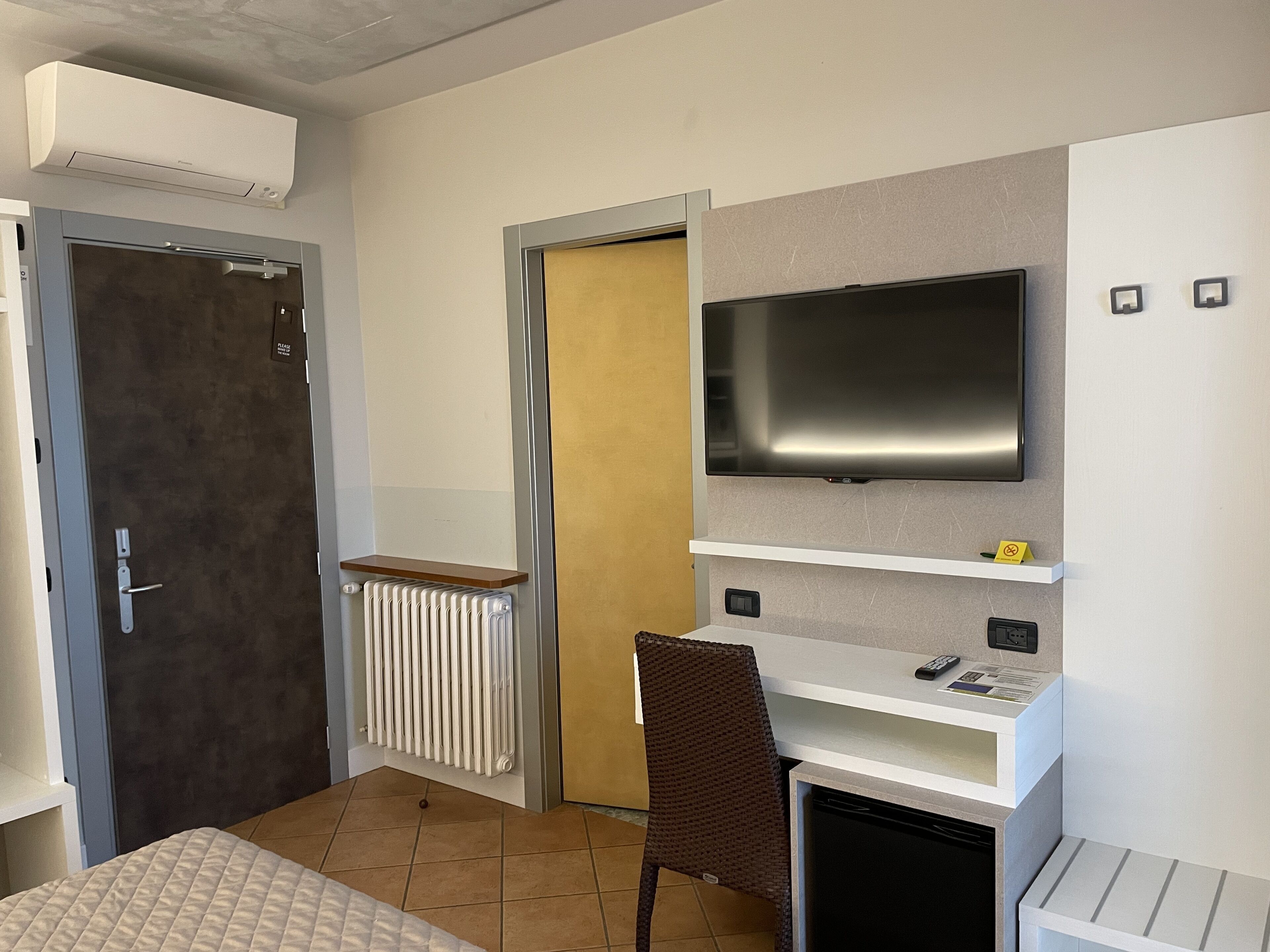A compact hotel room with a bed, a TV mounted on the wall, a small desk, and a chair.
