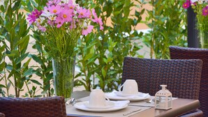 A dining table set with white plates, cups, and a lantern, surrounded by wicker chairs and a vase of pink flowers. - LH Hotel Lloyd Rome (Rome)
