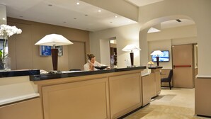 A hotel reception area with a counter, a TV, and a chair. - LH Hotel Lloyd Rome (Rome)