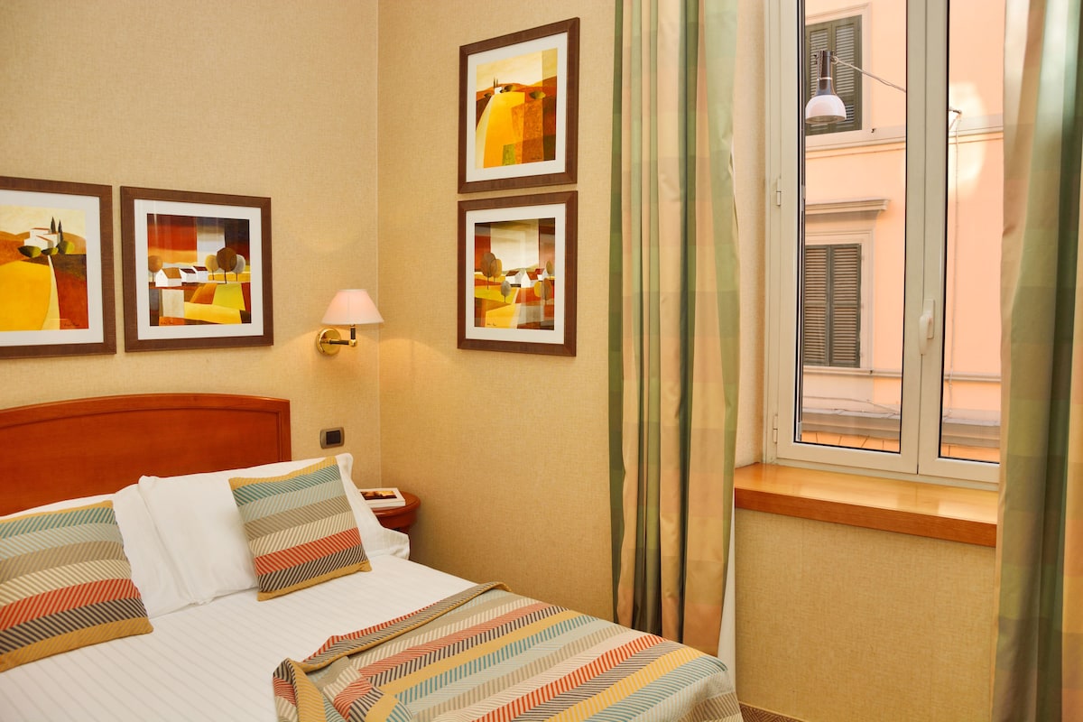 Una habitación de hotel con una cama, una mesita de noche, una lámpara y tres cuadros en la pared.