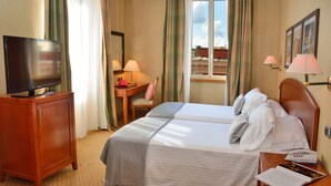 A hotel room with a bed, a desk, a television, and a window with curtains. - LH Hotel Lloyd Rome (Rome)