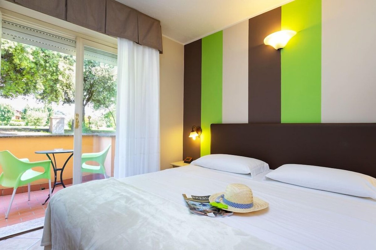 A hotel room with a bed, a window with curtains, a green chair, and a table.