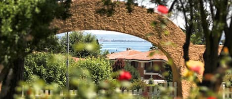 Un arco de piedra enmarca la vista de un pueblo costero con edificios y una extensión de agua.