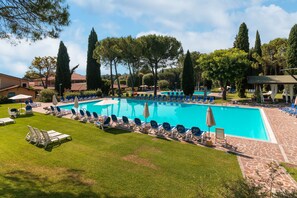A swimming pool with lounge chairs and umbrellas, surrounded by trees and a stone patio. - West Garda Hotel (Padenghe sul Garda)