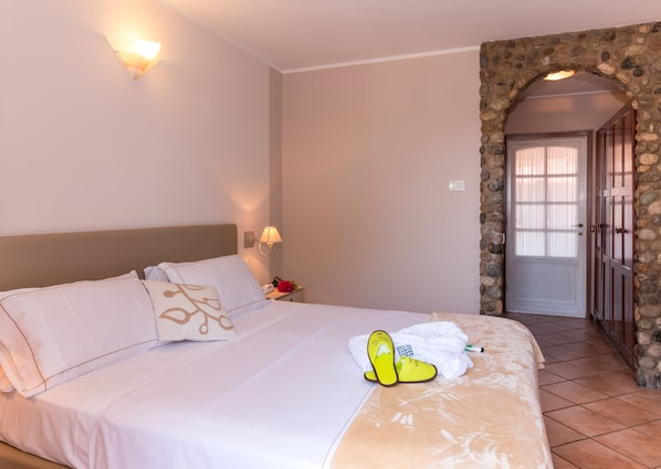 A hotel room with a bed, a nightstand, a lamp, and a stone wall. - West Garda Hotel (Padenghe sul Garda)