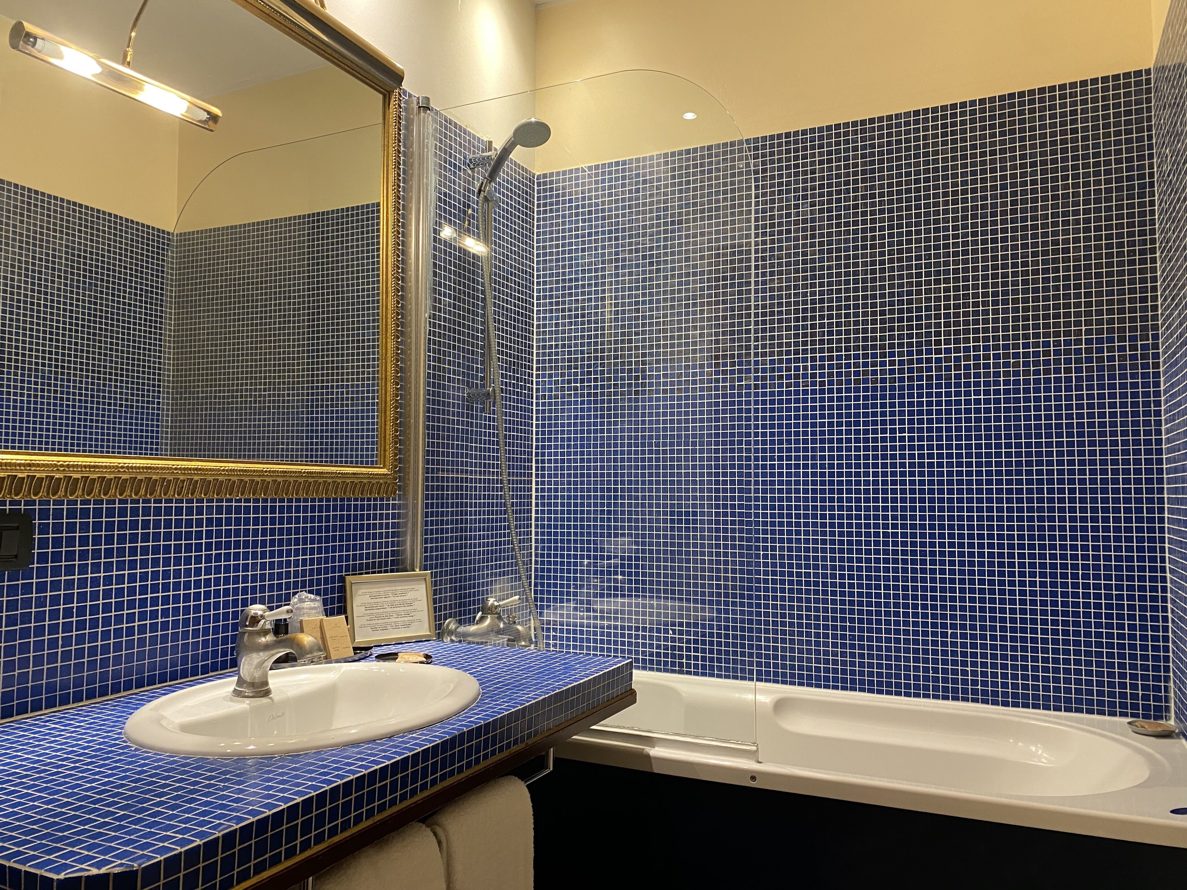 Une salle de bain avec des murs recouverts de carreaux bleus, un lavabo blanc et une baignoire.