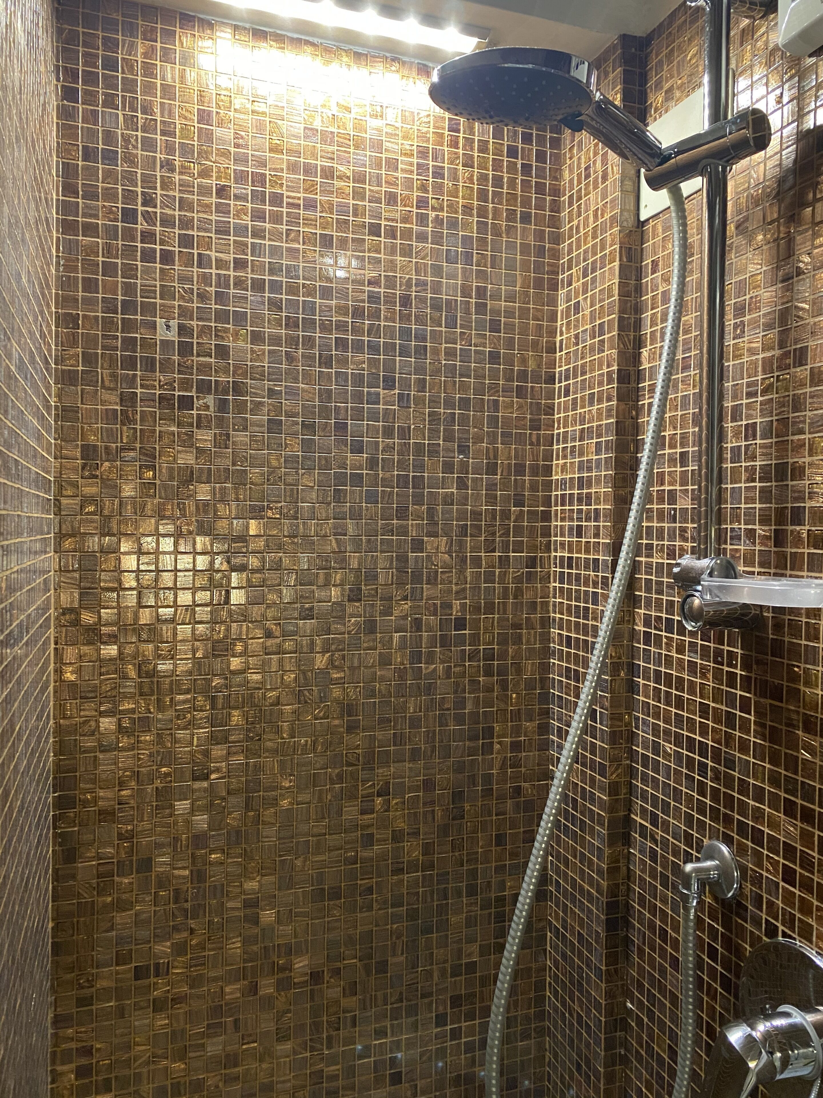 A shower with a tiled wall and a handheld showerhead.