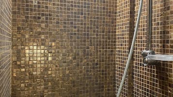 A shower with a tiled wall and a handheld showerhead.