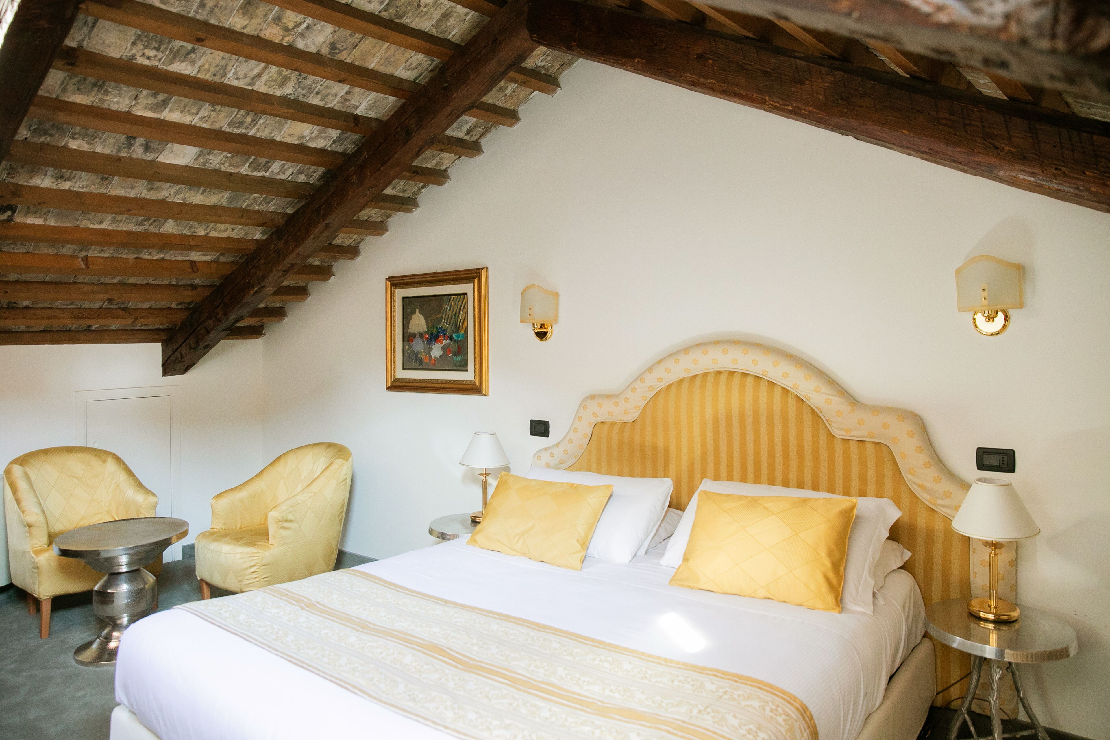A hotel room with a bed, two armchairs, a small round table, and a ceiling with exposed wooden beams.