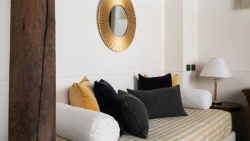 A neatly made bed with striped bedding, a round mirror with a gold frame, and a bedside lamp.