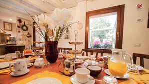 Une table de petit-déjeuner dressée avec différents plats, un vase de fleurs et une vue sur l’extérieur par la fenêtre.