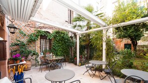 Une terrasse extérieure avec des tables et des chaises, entourée de verdure et d’un mur de briques.