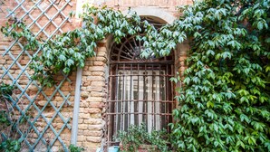 Un bâtiment rustique doté d’un portail en métal, d’un mur en briques et d’une fenêtre avec une grille en métal.