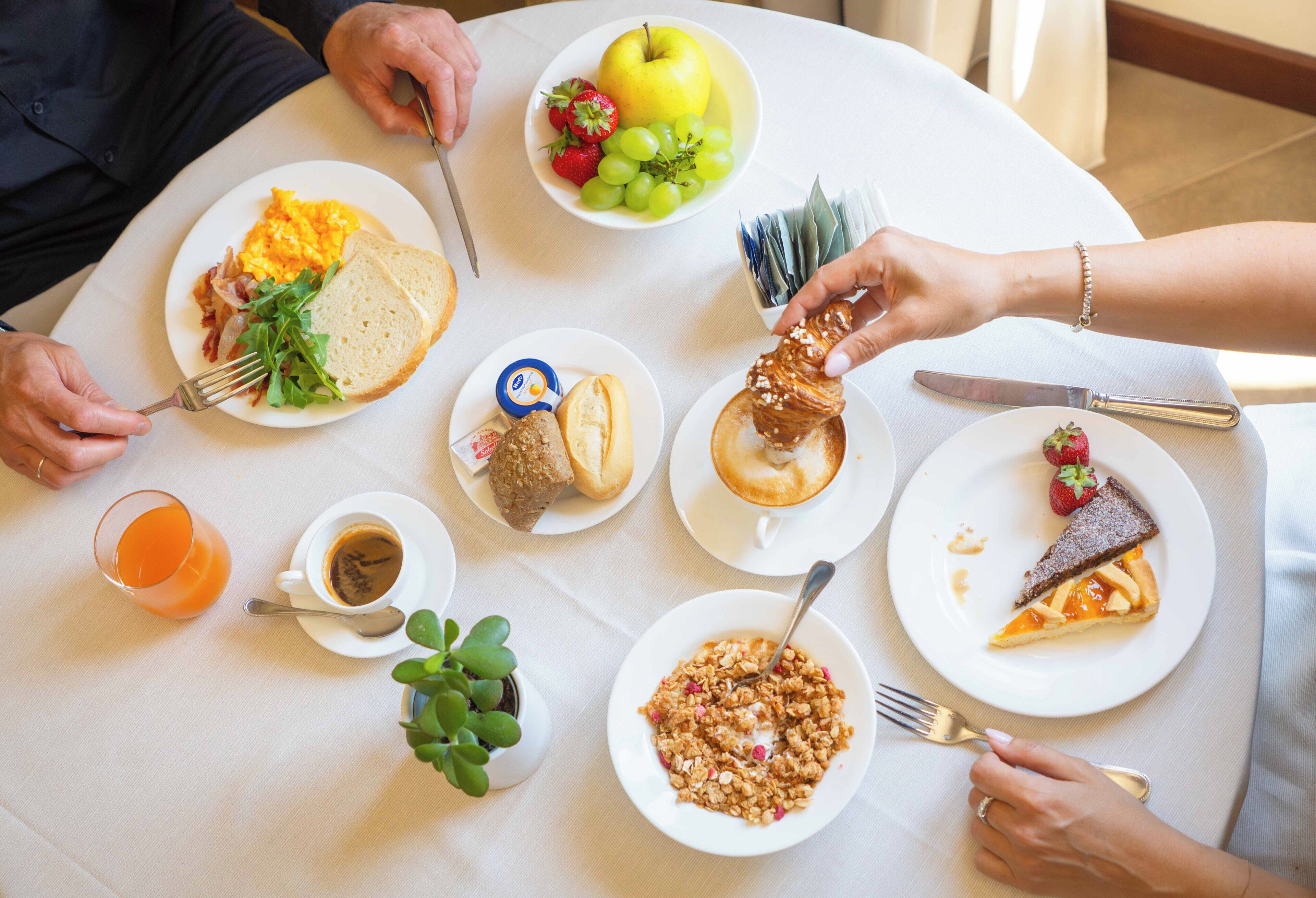Une table à manger avec divers aliments pour le petit-déjeuner, notamment des œufs, des toasts, des fruits et des viennoiseries.