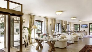 Un salón amplio con una mesa de centro de cristal, sofás blancos y un ventanal con cortinas.