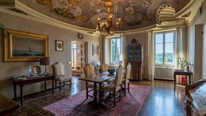 Una sala imponente con un gran candelabro ornamentado, una mesa de comedor con sillas y un tapete rojo con estampado.