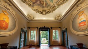 Una sala imponente con frescos ornamentales en el techo, ventanas amplias y vistas a un jardín.