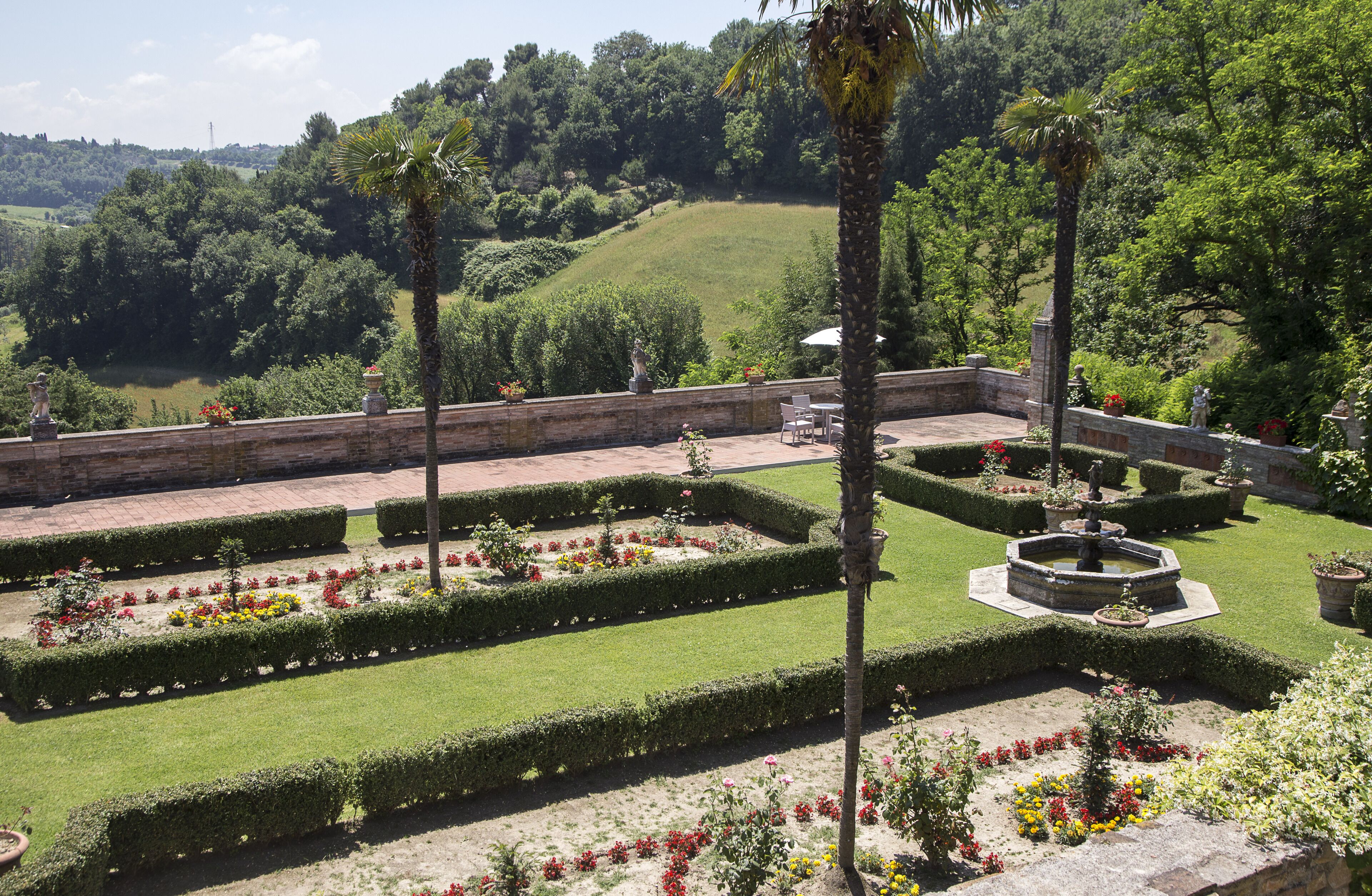 Um jardim formal com sebes bem cuidadas, uma fonte central e uma área de estar.