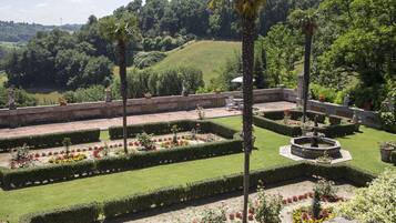 Um jardim formal com sebes bem cuidadas, uma fonte central e uma área de estar.
