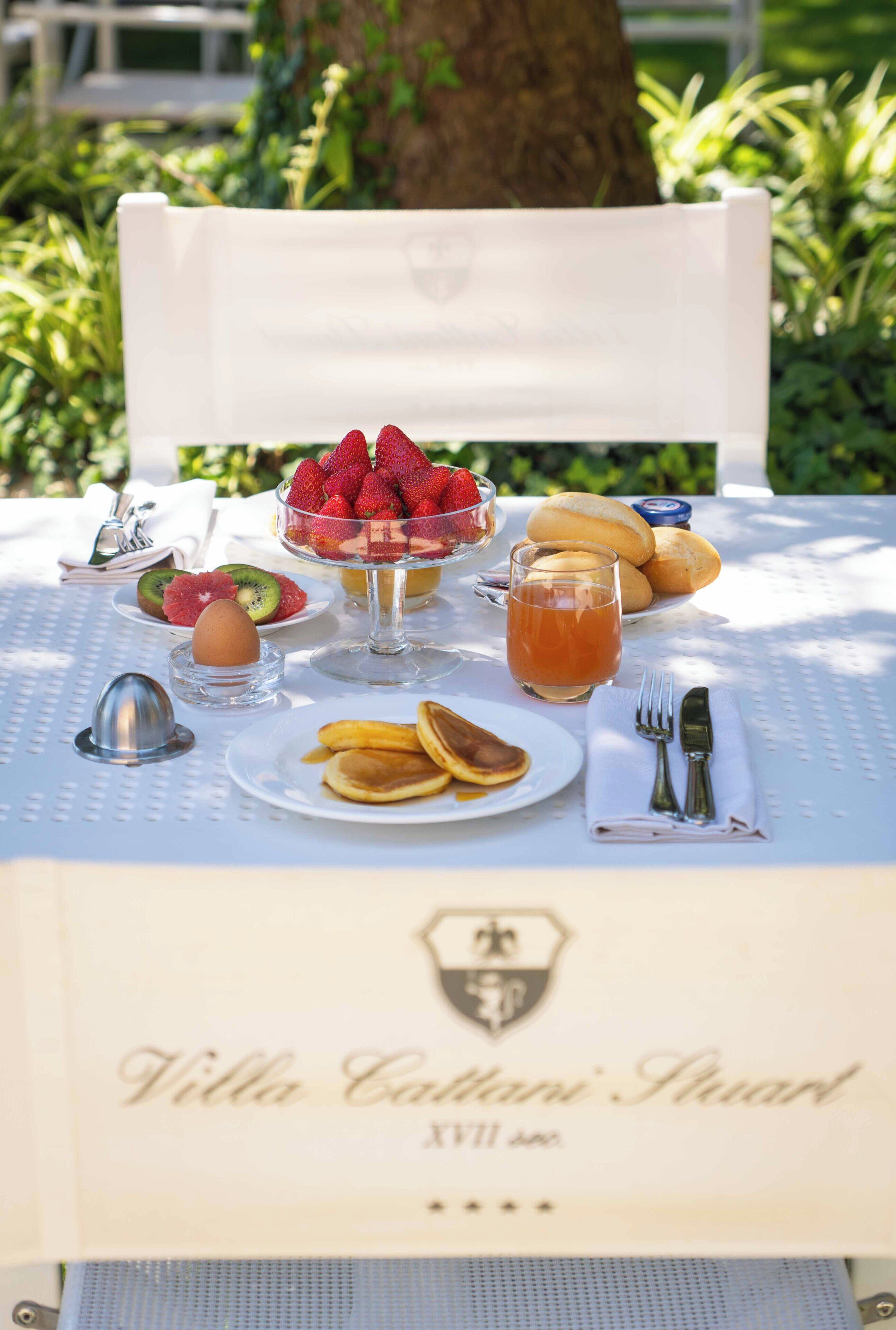 Ein Esstisch ist reichhaltig mit Frühstücksleckereien gedeckt, darunter Pfannkuchen, Obst und ein Glas Saft.