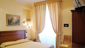 Une chambre d’hôtel avec un grand lit, une table de chevet en bois, une lampe, un tableau au mur et une fenêtre avec des rideaux.