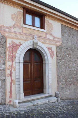 Fachada de edifício com uma grande porta de madeira arqueada, uma janela acima e decoração na parede incluindo uma trepadeira e um leão.