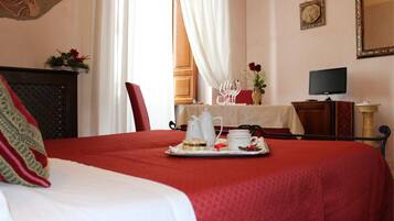 A hotel room with a bed, a tray of breakfast items, a television, and a painting on the wall.