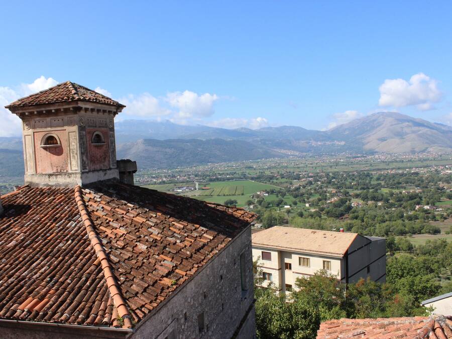 A building with a tiled roof and a bell tower, overlooking a valley with mountains in the background.