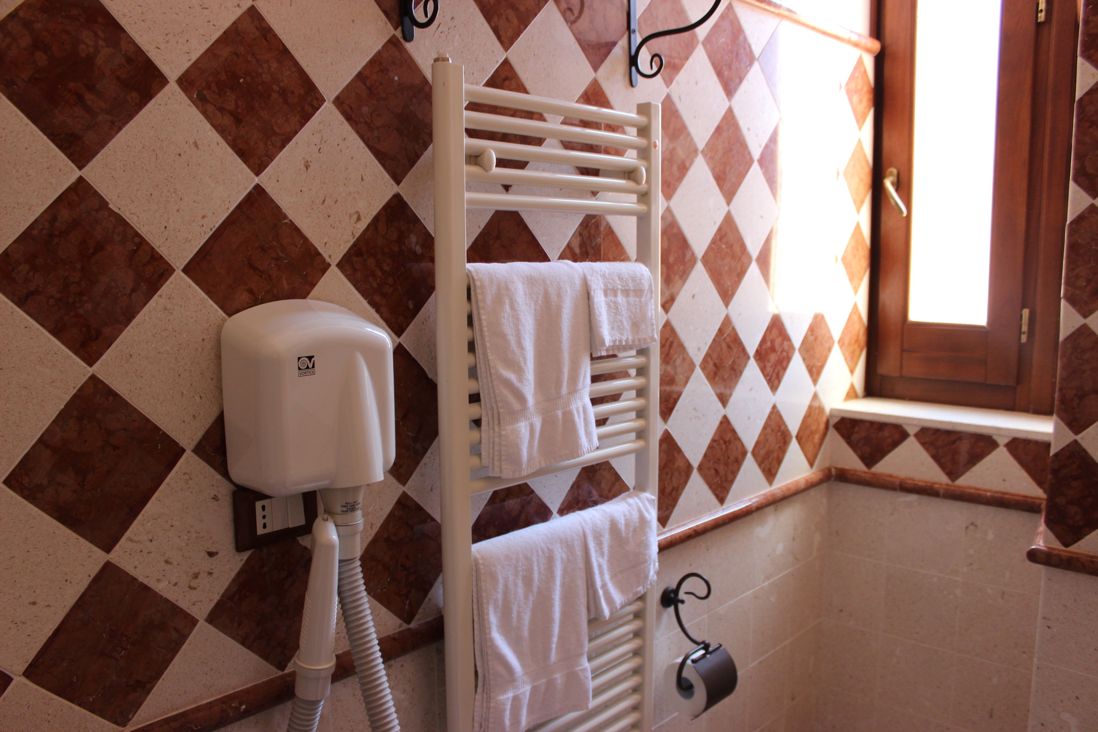A bathroom with a white towel rack, a hand dryer, and a window with a view of the outside.