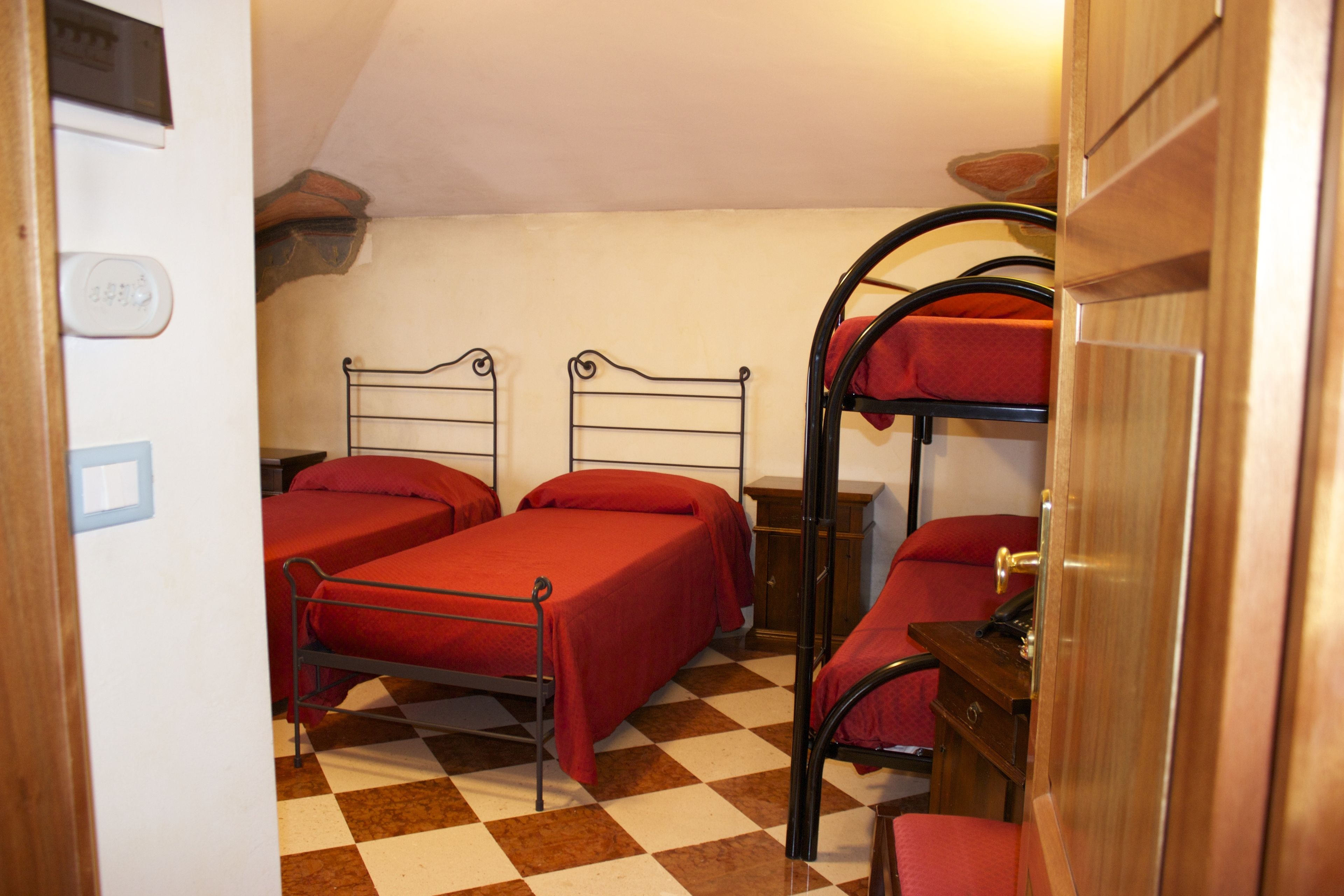 Ein Zimmer mit zwei Einzelbetten und einem Etagenbett, Linoleumboden, Holztür und einem kleinen Schrank.